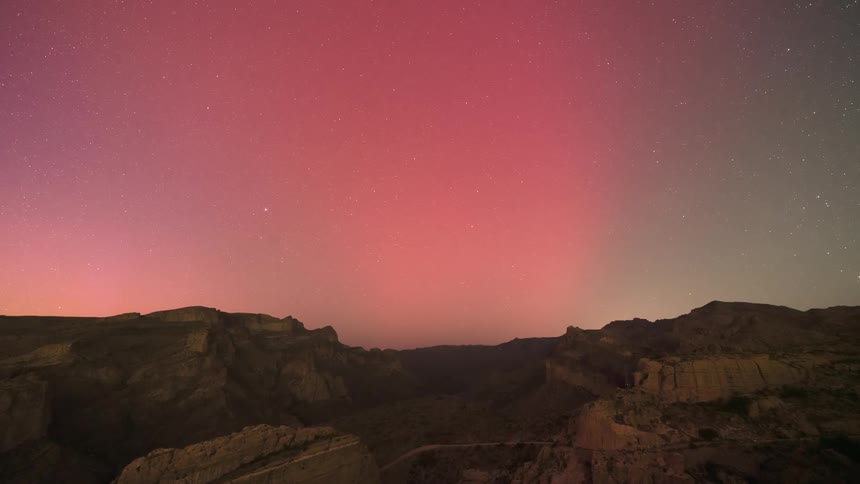 A bright pink aurora in the night sky over desert mountains