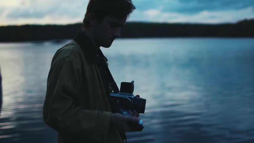 A young man standing by a lake uses a light meter to take a photograph