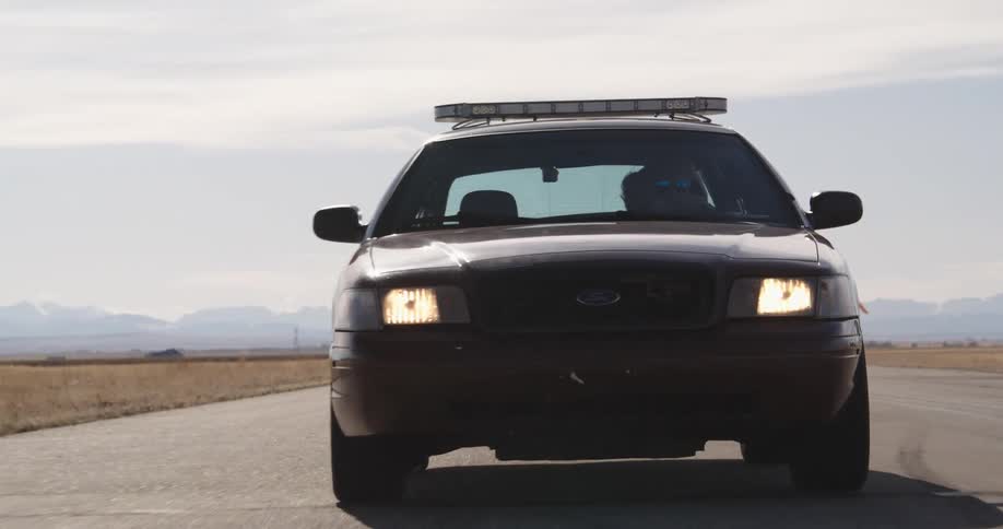 A red ford crown victoria police interceptor drives off on an empty tarmac in the countryside