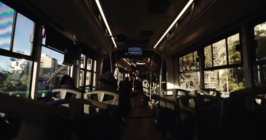 Inside a bus people are seated engaged in conversations and looking out the windows as the vehicle moves along its route