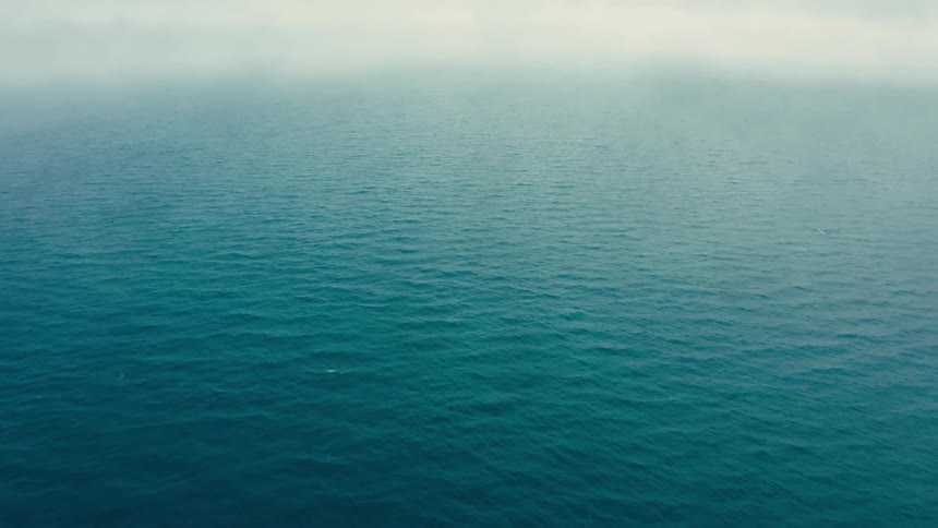 The vast ocean shows tiny rippling waves from an aerial view above