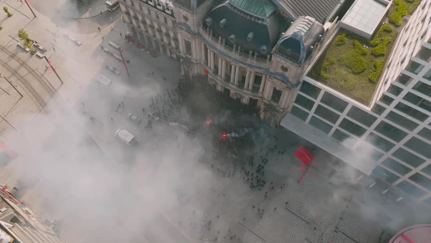 A protest is happening outside a building with a flare and a poster life goes on around that protest