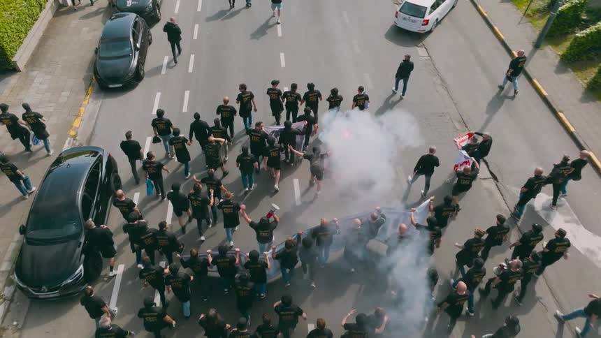 A riot of several people wearing black clothes and holding a flare giving off smoke and they are walking on an asphalt street