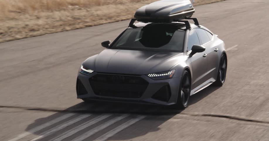 An audi rs7 with a roof rack drives on an open road