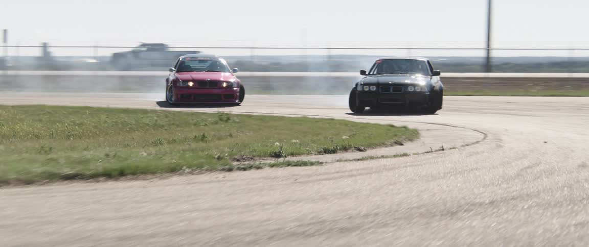Two cars racing on a track drifting around a corner