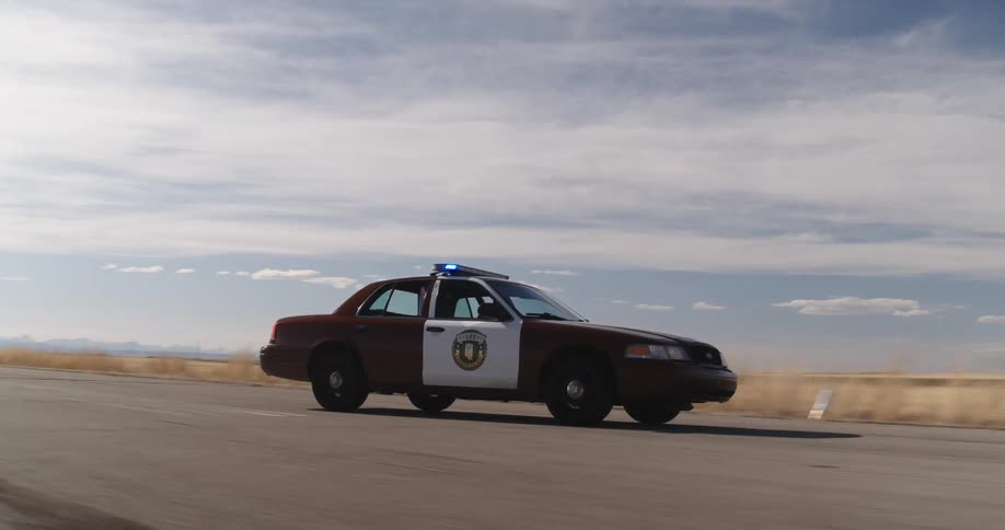 A police car is swerving all over the road in a desolate grass covered flatland