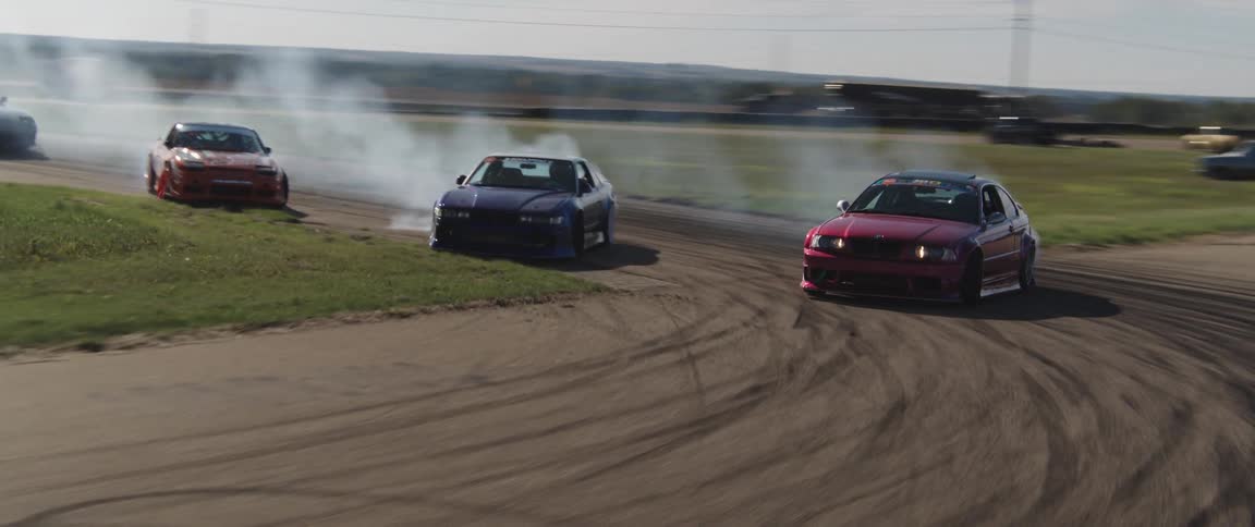 Aerial view of cars drifting on a racetrack leaving visible tire smoke behind them
