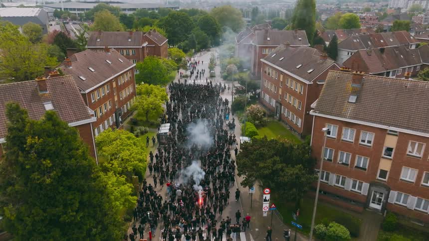 A huge crowd of people wearing all black marches down the street of a small town with identical houses