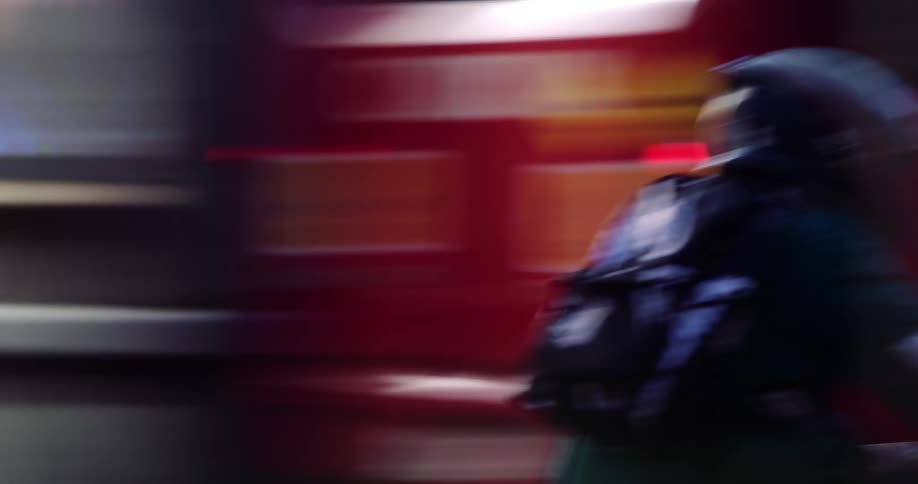 A person wearing a helmet and backpack driving a motorcycle quickly on a street