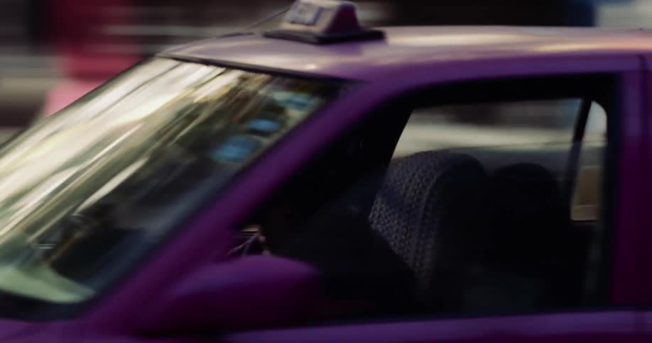 A closeup of a moving pink taxi cab driving in the city