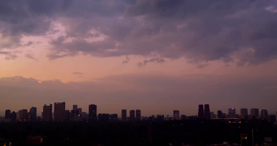 A city is shown at dusk under a cloudy purple sky above silhouetted buildings