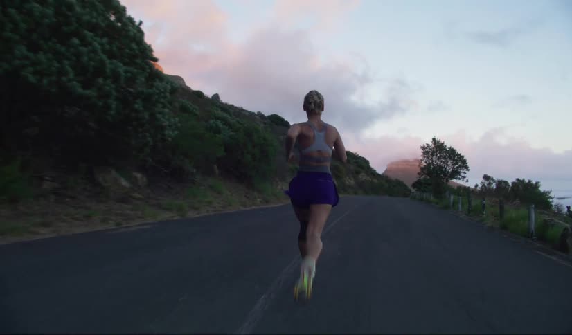 Woman running on a paved road surrounded by vegetation and mountains at dusk