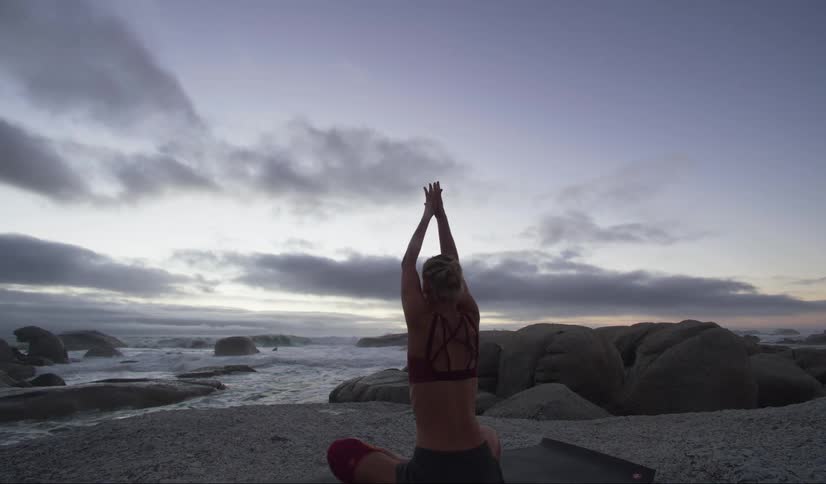 A woman raising her arms up while sitting doing yoga and meditation pose in front of the sea