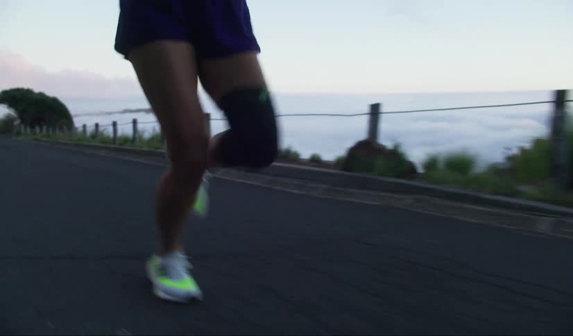 Legs of a woman running on a road with hills around