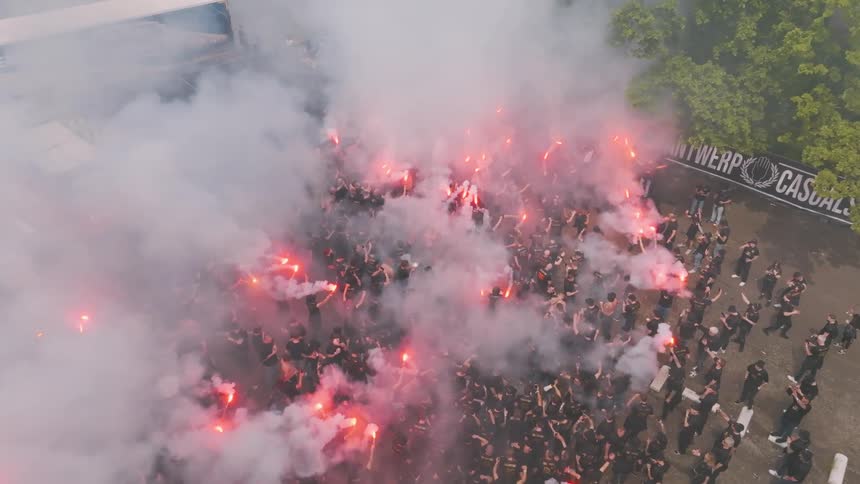 Aerial view of a group of people gathered in an outdoor space some of them holding red flares that emit smoke