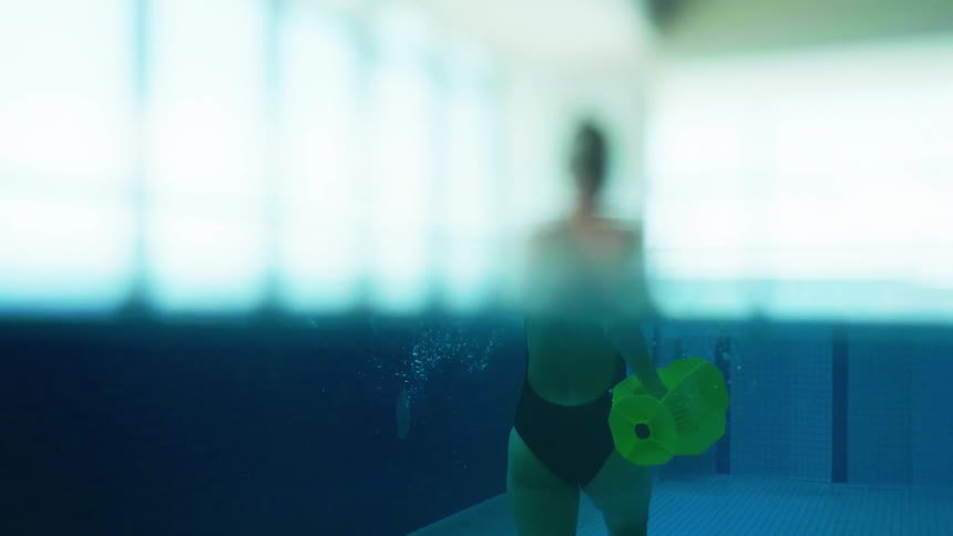 Blurred person walking in a swimming pool carrying weight in hands