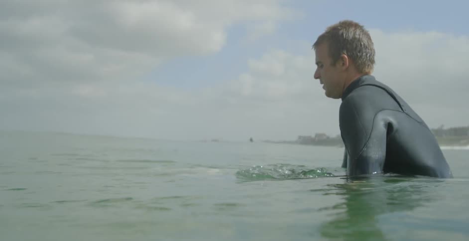 A male surfer is sitting in the ocean waiting for a wave