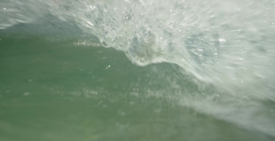 Wave rolling forward and overcoming the camera at water level on a partly cloudy day