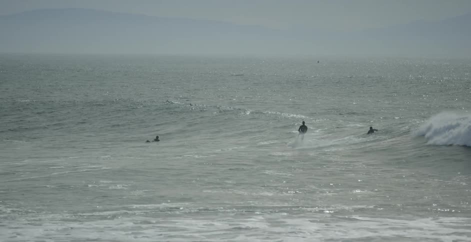 A surfer rides a wave while others paddle out