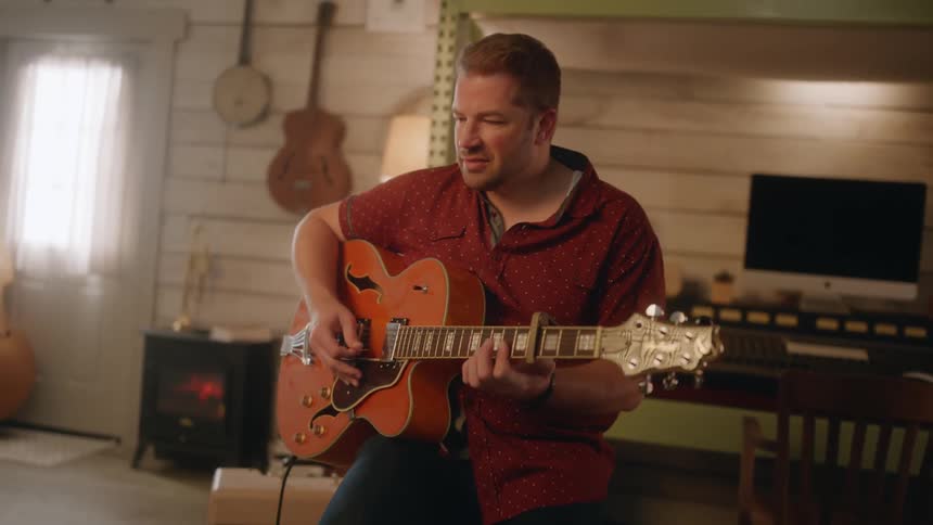 A man sitting on a bench nodding his head while playing guitar
