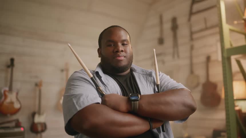 Percussionist in a music studio with arms crossed holding drumsticks