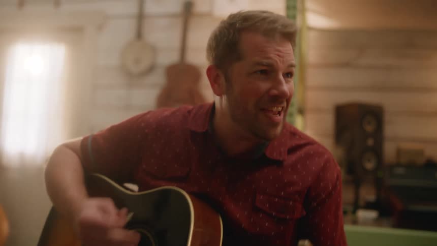 A guitarist passionately strums his guitar and sings with his bandmates