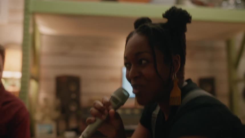 Smiling woman singing in a studio with the microphone and next to her a man playing the guitar