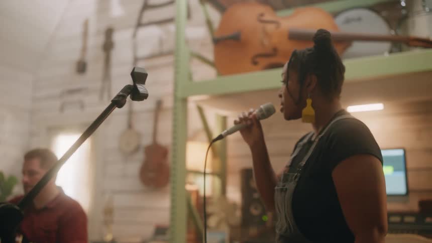 A singer confidently delivering her performance into the microphone while her bandmates play their instruments in the background