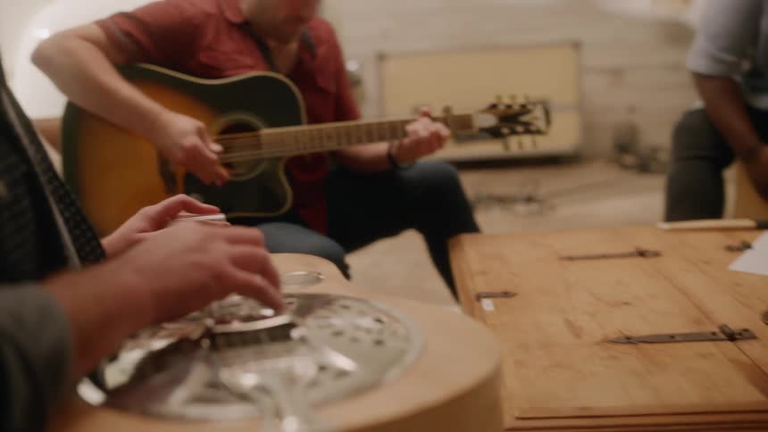 Band of four people sitting in a studio singing and playing