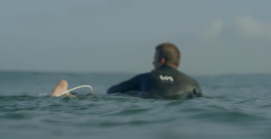 A surfer is paddling his surfboard on a sunny day