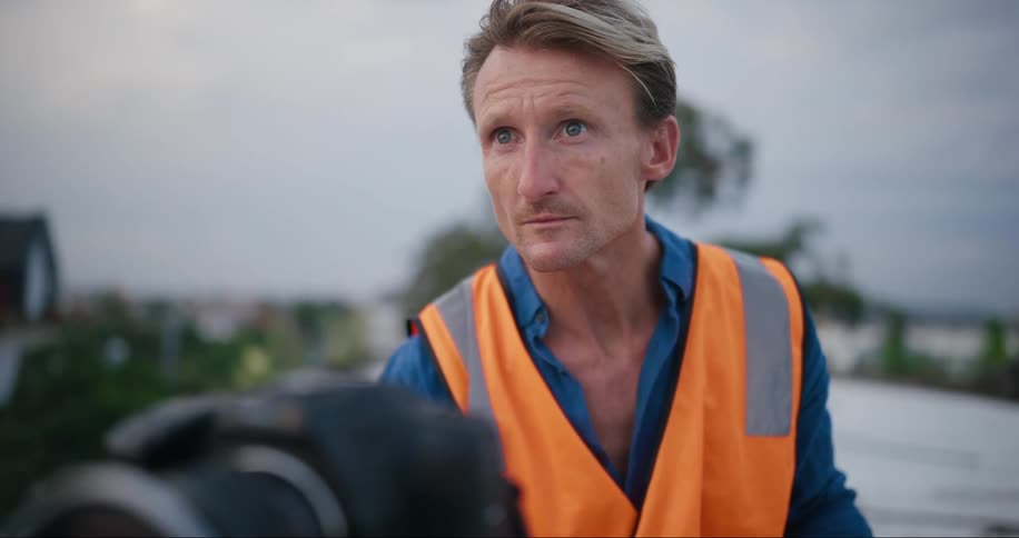 Man in an orange safety vest is looking at the camera and checking something