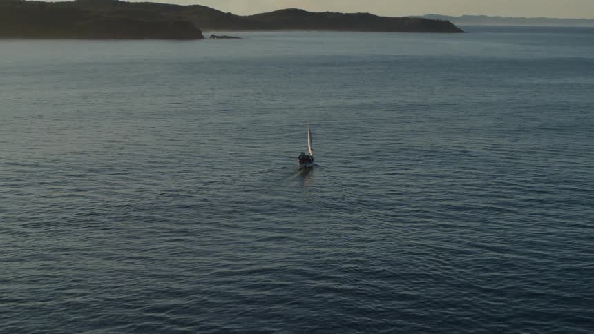 A white sailboat with its sails up floats on calm water