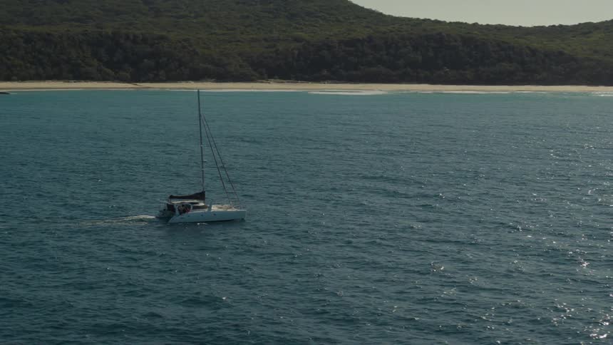 Sailboat moves through reflective waters off the shore using their motor