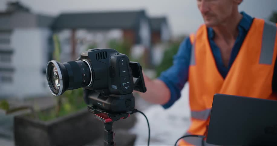Man in orange reflective vest operating a professional camera with an open laptop