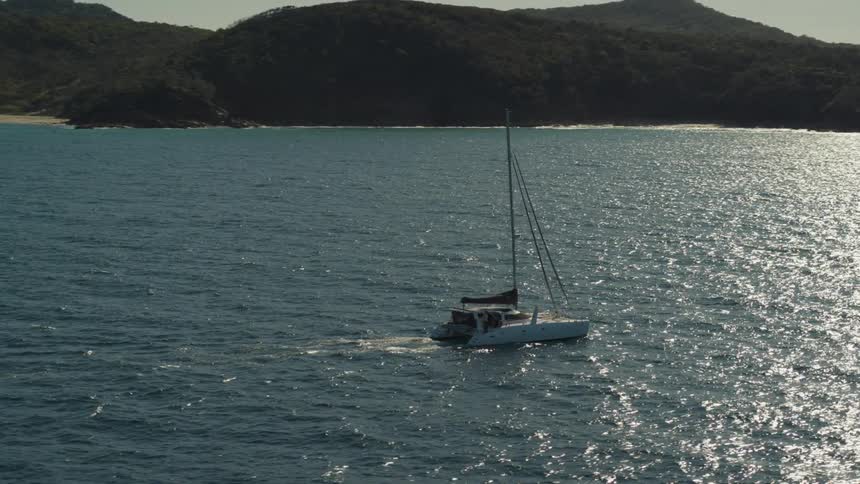 Aerial view of a sailboat sailing across water at sunset