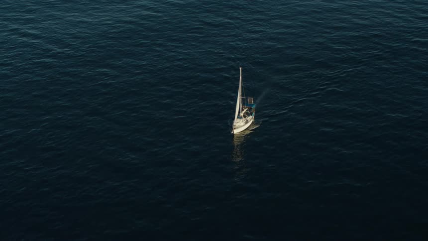Sailboat sails through blue tinted water leaving a wake