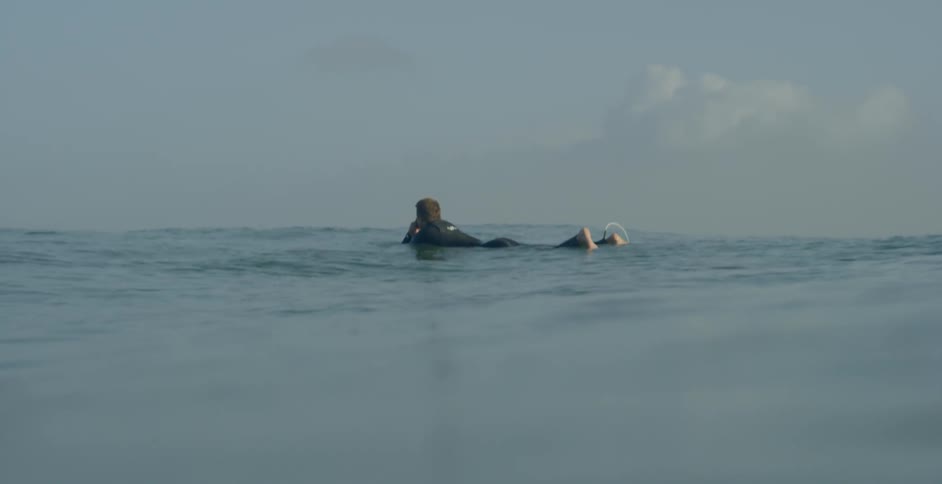 A person in a wetsuit lies floating on a surfboard in the ocean