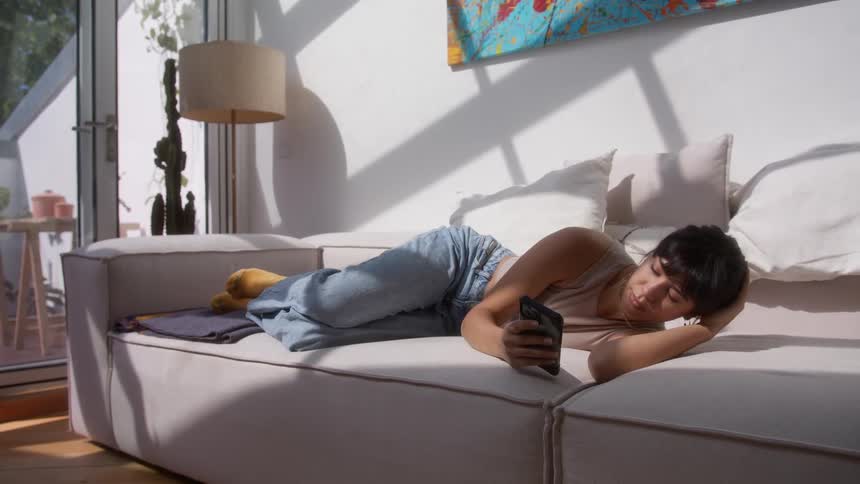 Woman lying on a wide couch checks her smartphone