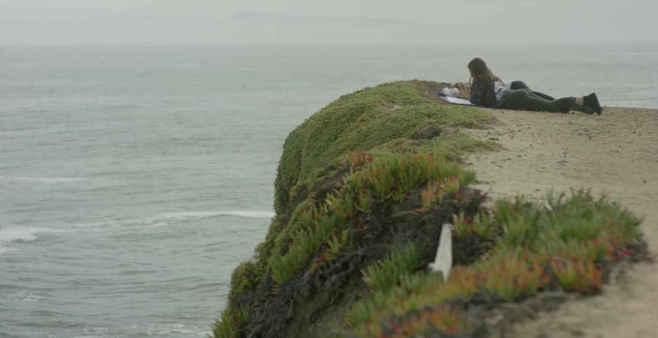 Two women laying at the edge of cliff overlooking ocean
