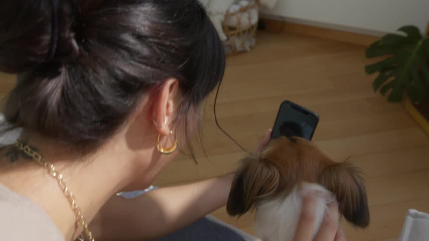 Woman sits and talks with a friend via a video call while petting her dog
