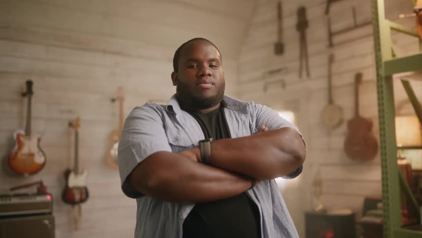 A percussionist with arms crossed in a musical studio surrounded by instruments