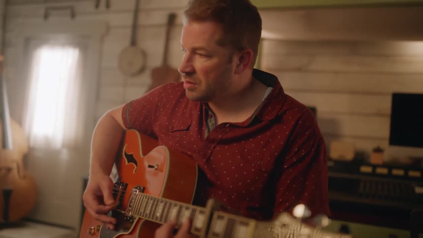 Bearded man wearing a red shirt plays the guitar