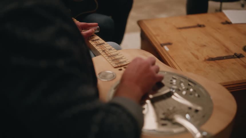 Man strumming guitar in a studio filled with musical equipment