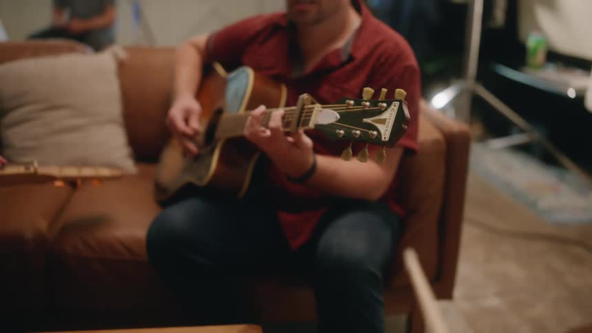 Two people sitting with one of them playing guitar and the other with drumsticks