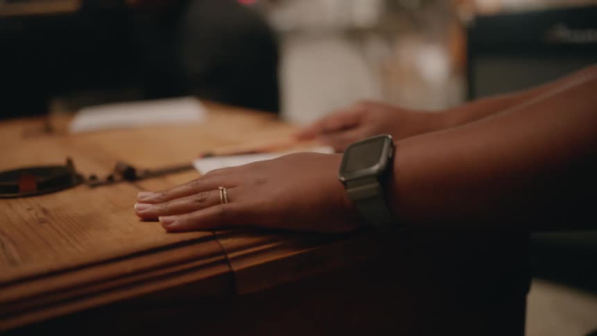 A black woman taps her fingers and a pencil on a wooden chest