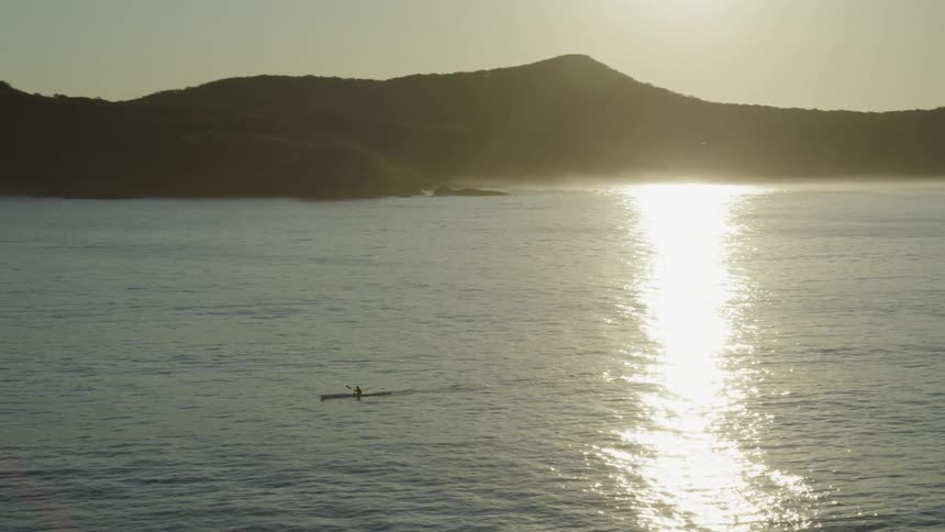 Aerial panorama and the silhouette of a person traveling in the middle of the sea with a canoe and the silhouette of mountains on the horizon