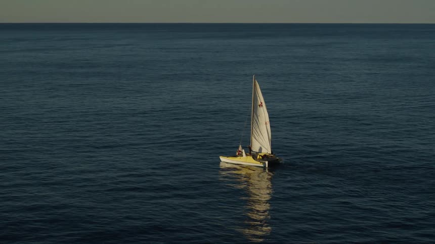 The small sailboat is dwarfed by the vastness of the ocean
