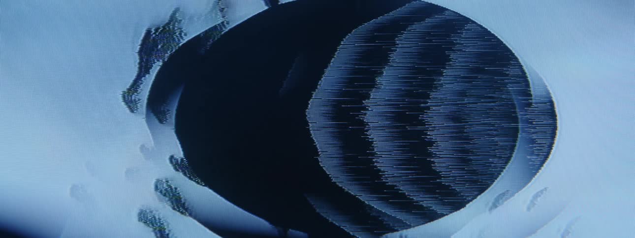 Flickering image of smudges flowing past dark ovals partially covered by concentric rings plays on screen
