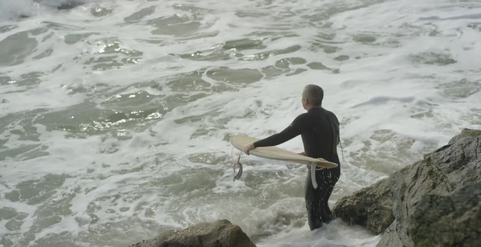 Surfer climbs carefully down rocky cliff into ocean