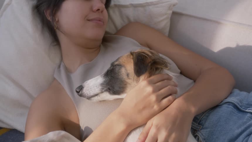 Woman cuddles and kisses dog while lying down